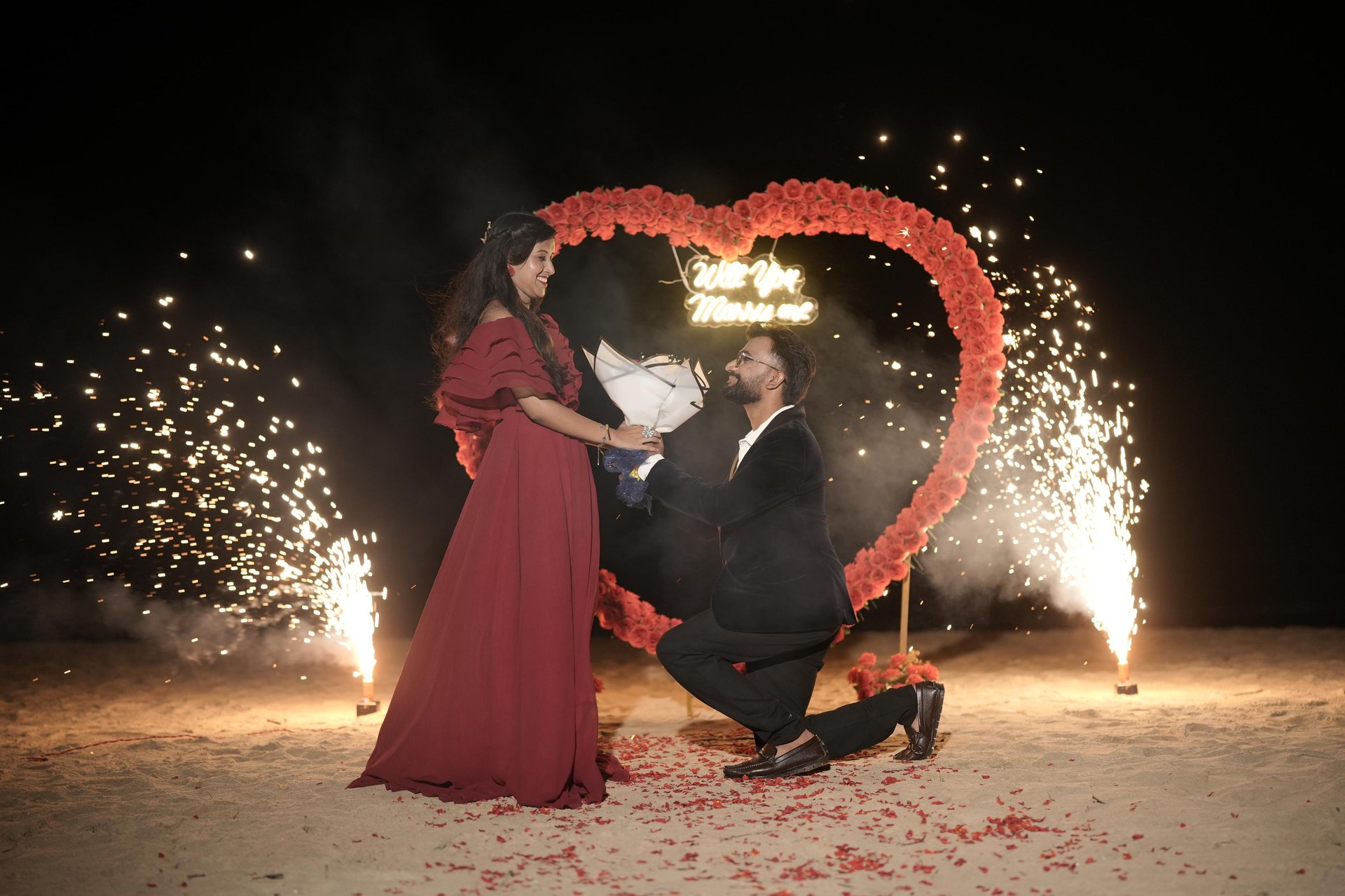 Purushotham proposing to Nikitha beside a rose heart arch at night